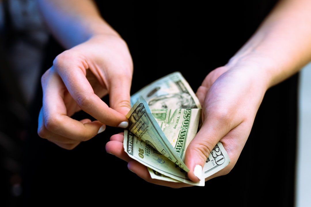 Hands counting a stack of US twenty-dollar bills against a dark background.