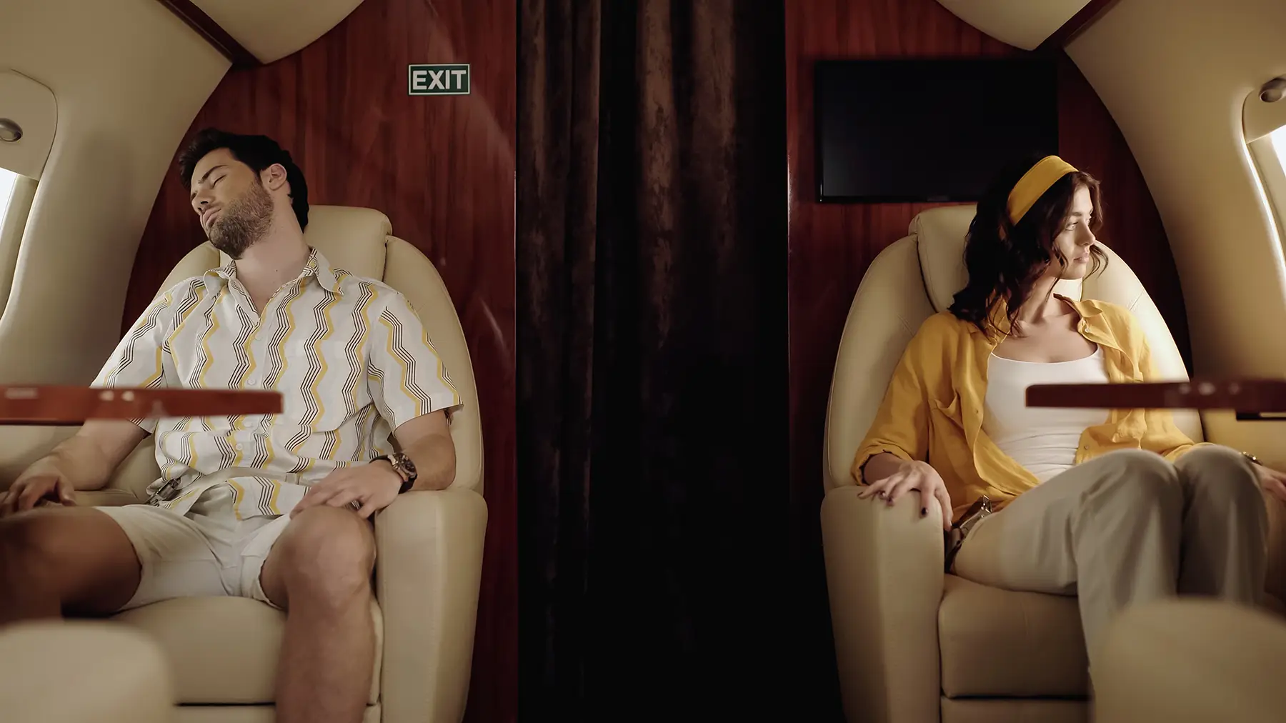 Couple in a private jet: man sleeping, woman looking out window, both wearing casual clothes.
