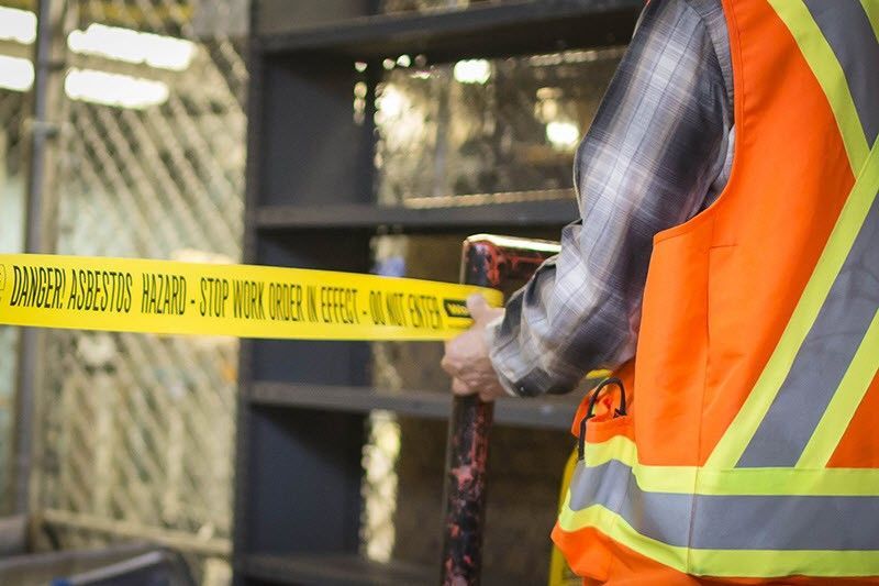 A man in an orange vest is holding a yellow tape that says danger.