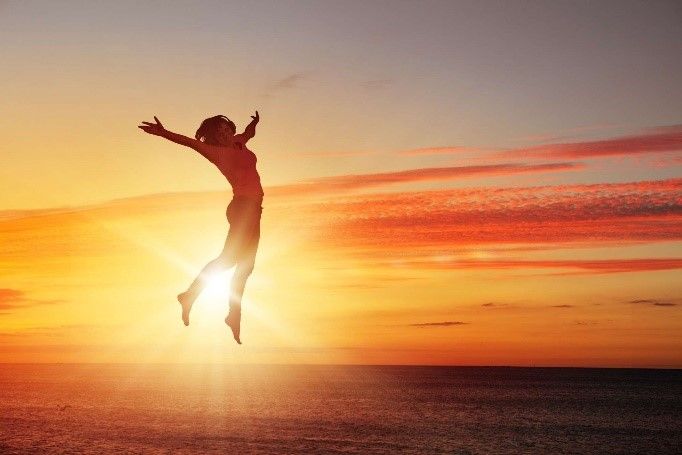 A woman is jumping in the air at sunset over the ocean.