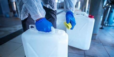 A person wearing blue gloves is holding a plastic container in a factory.