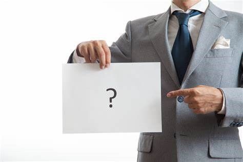 A man in a suit and tie is holding a piece of paper with a question mark on it.