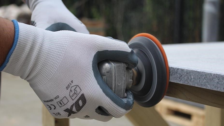 A person wearing a pair of gloves is using a grinder to polish a piece of granite.