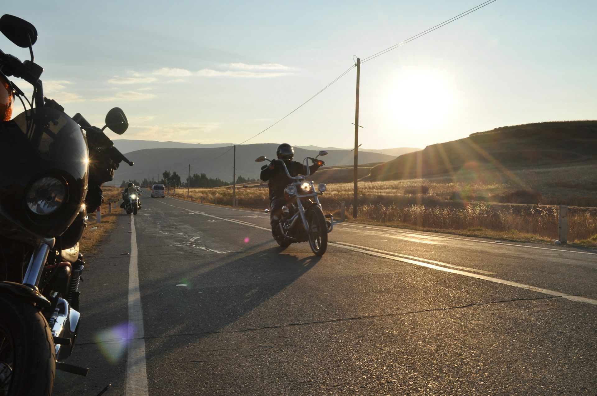 Motorcyclists riding on a sunlit road at sunset with hills in the background