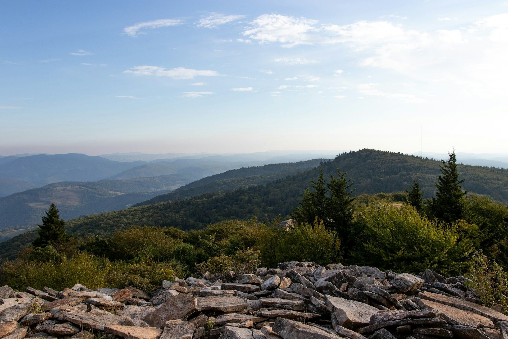 Rocky overlook with forested mountains and a hazy valley under a bright blue sky