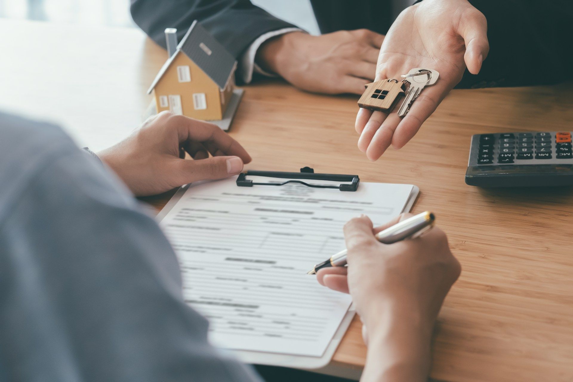 Hands reviewing a house sale contract at a desk with a calculator and model home