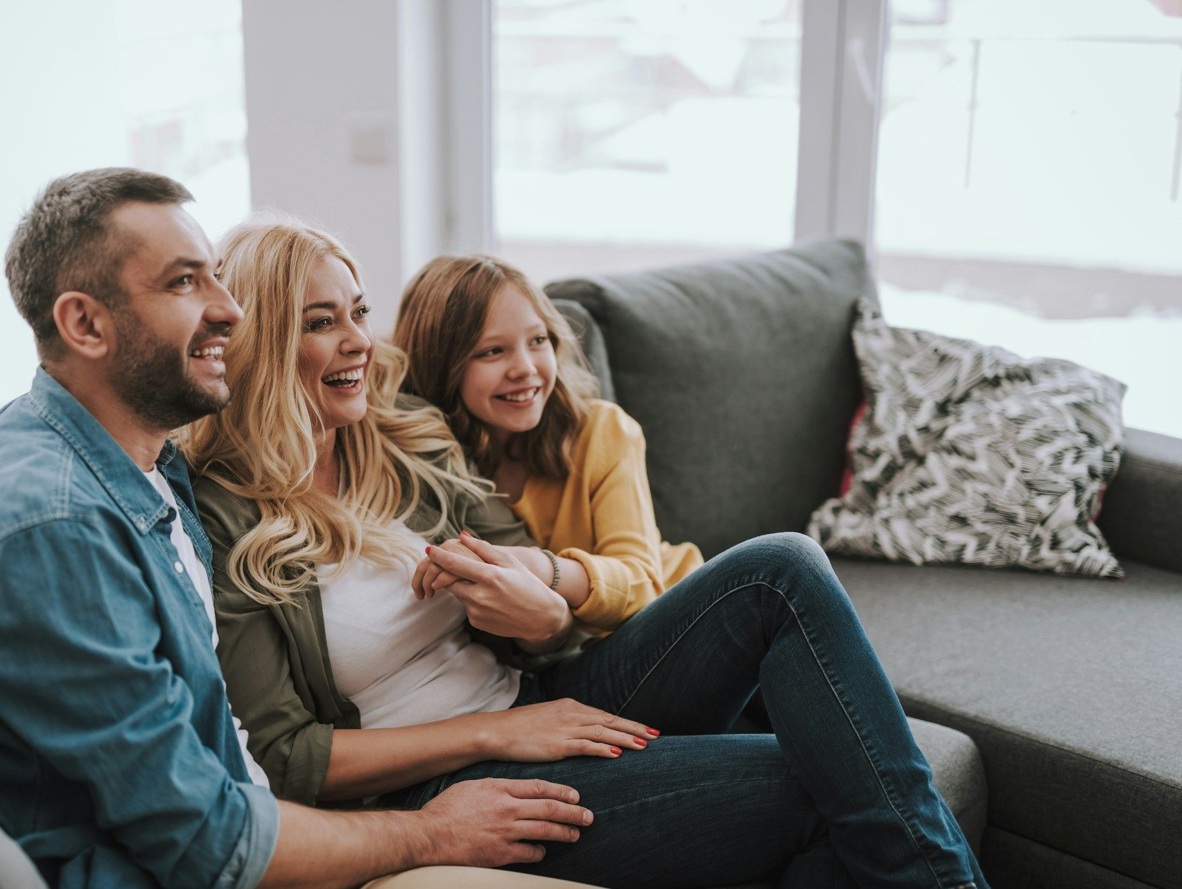 Three people smiling on a couch in a bright living room