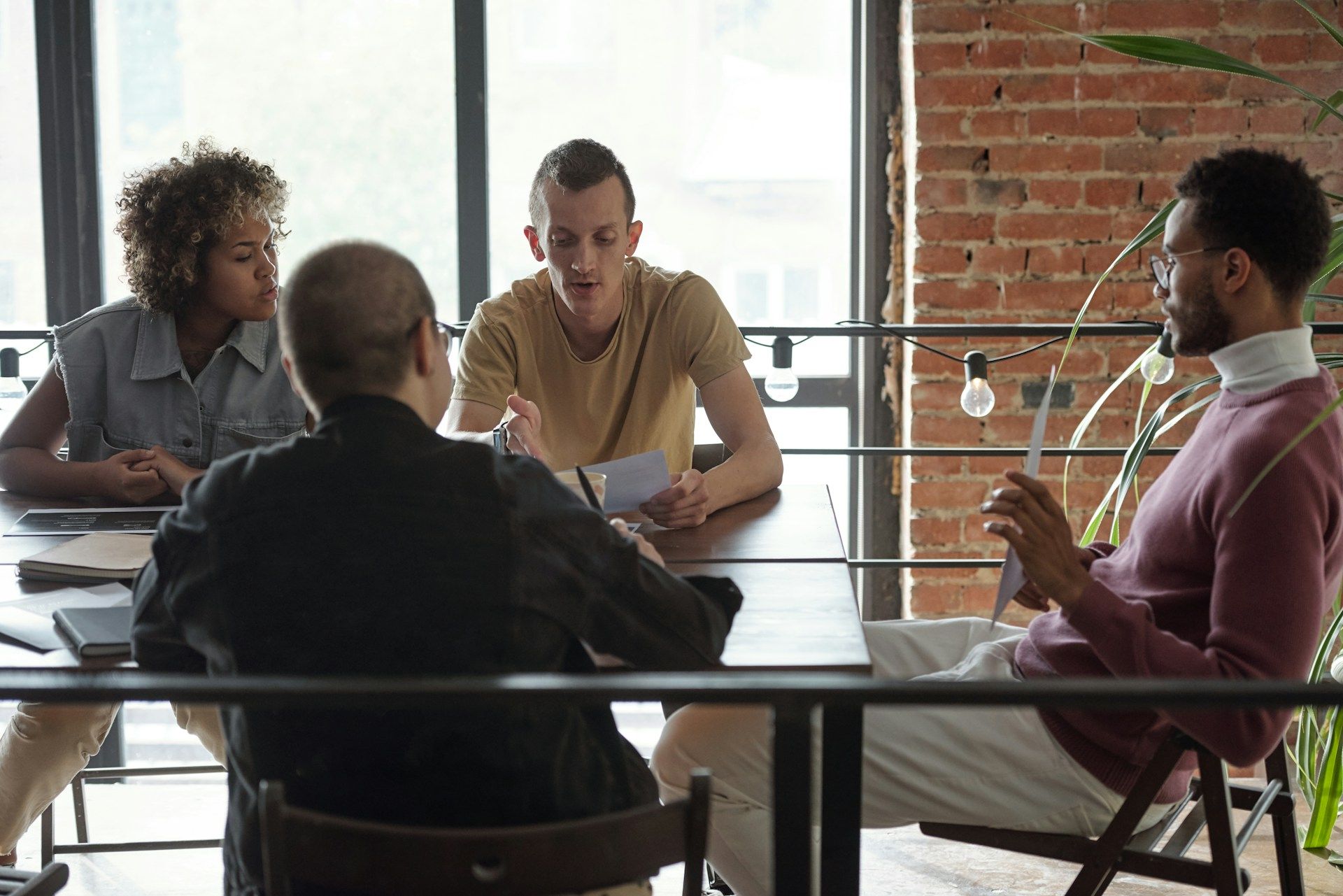 People in a meeting around a table in a bright office with brick walls and large windows