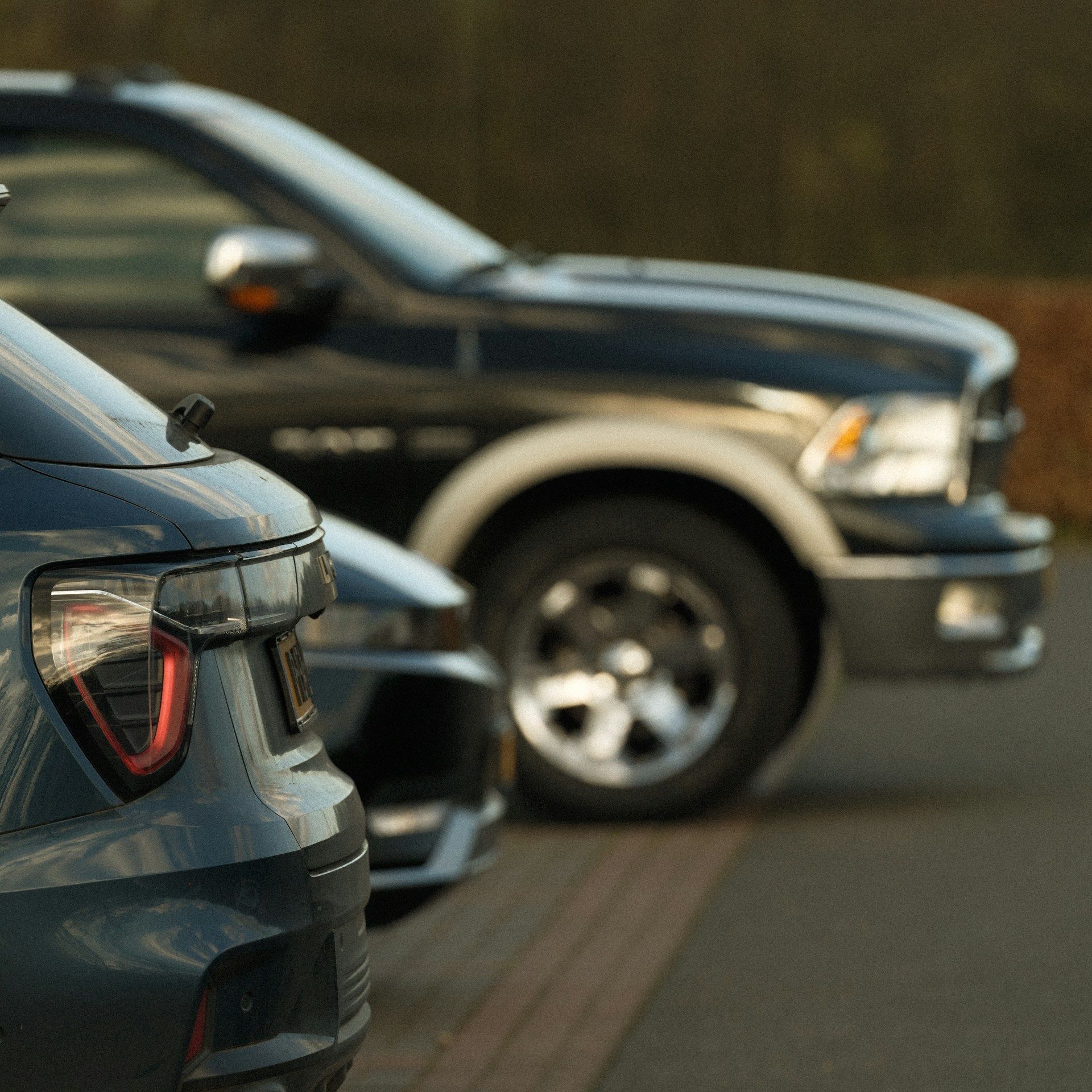 Two parked vehicles on a street, with a dark blue car in the foreground and a black pickup behind it.