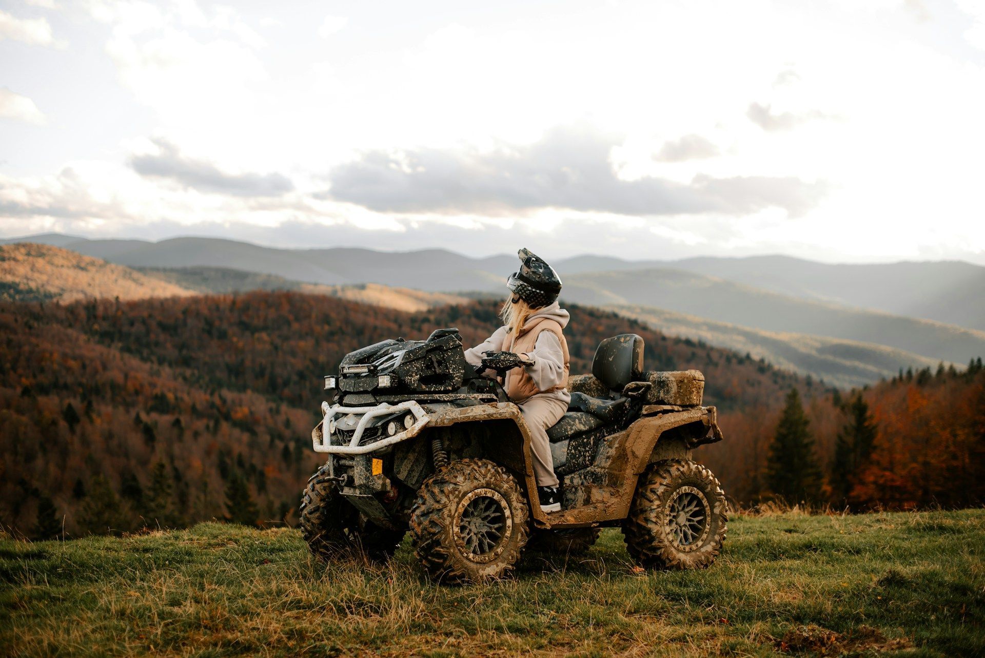Person riding an ATV in a grassy mountain landscape at sunset