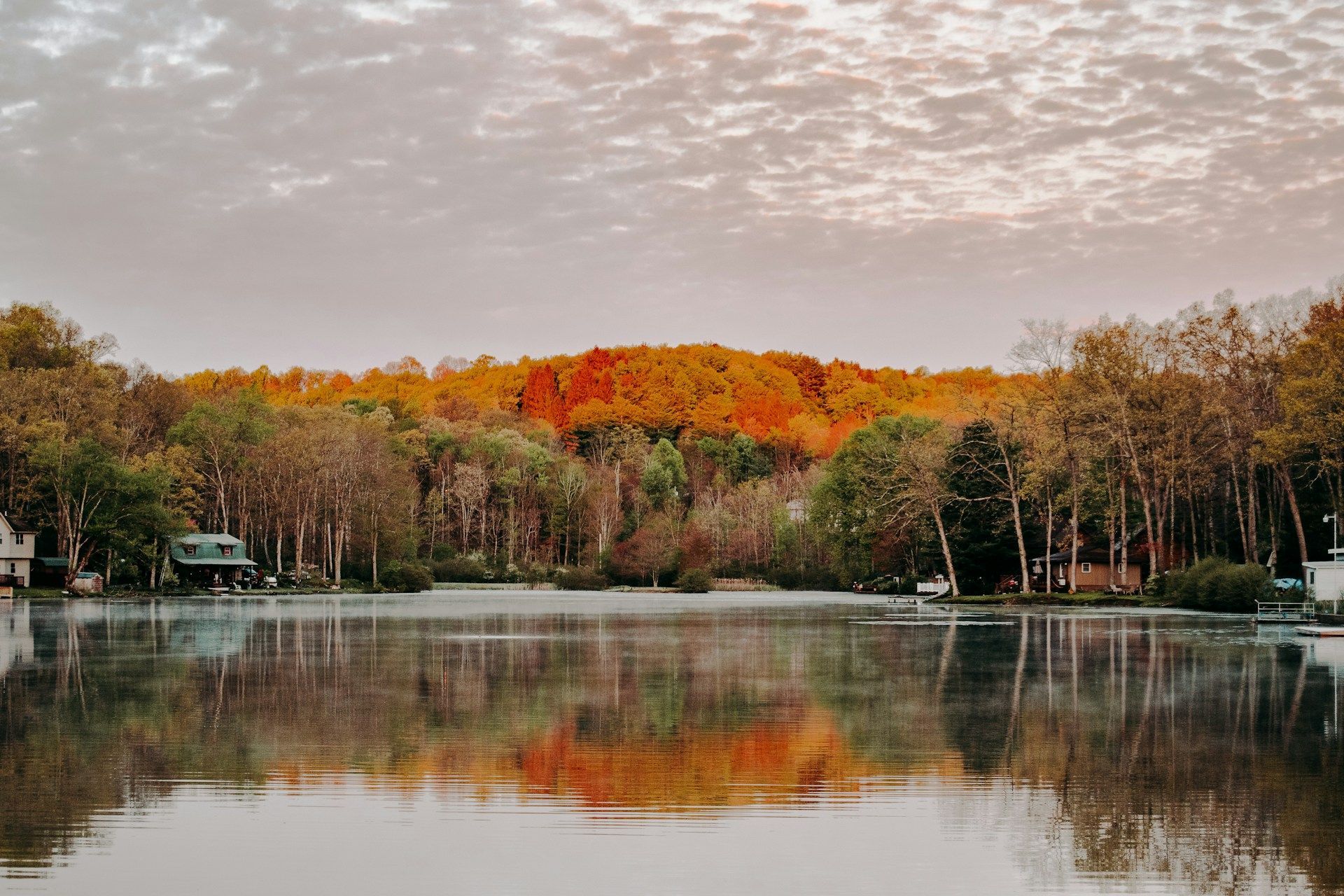 Calm lake reflecting autumn trees under a cloudy sky, with small docks along the shore