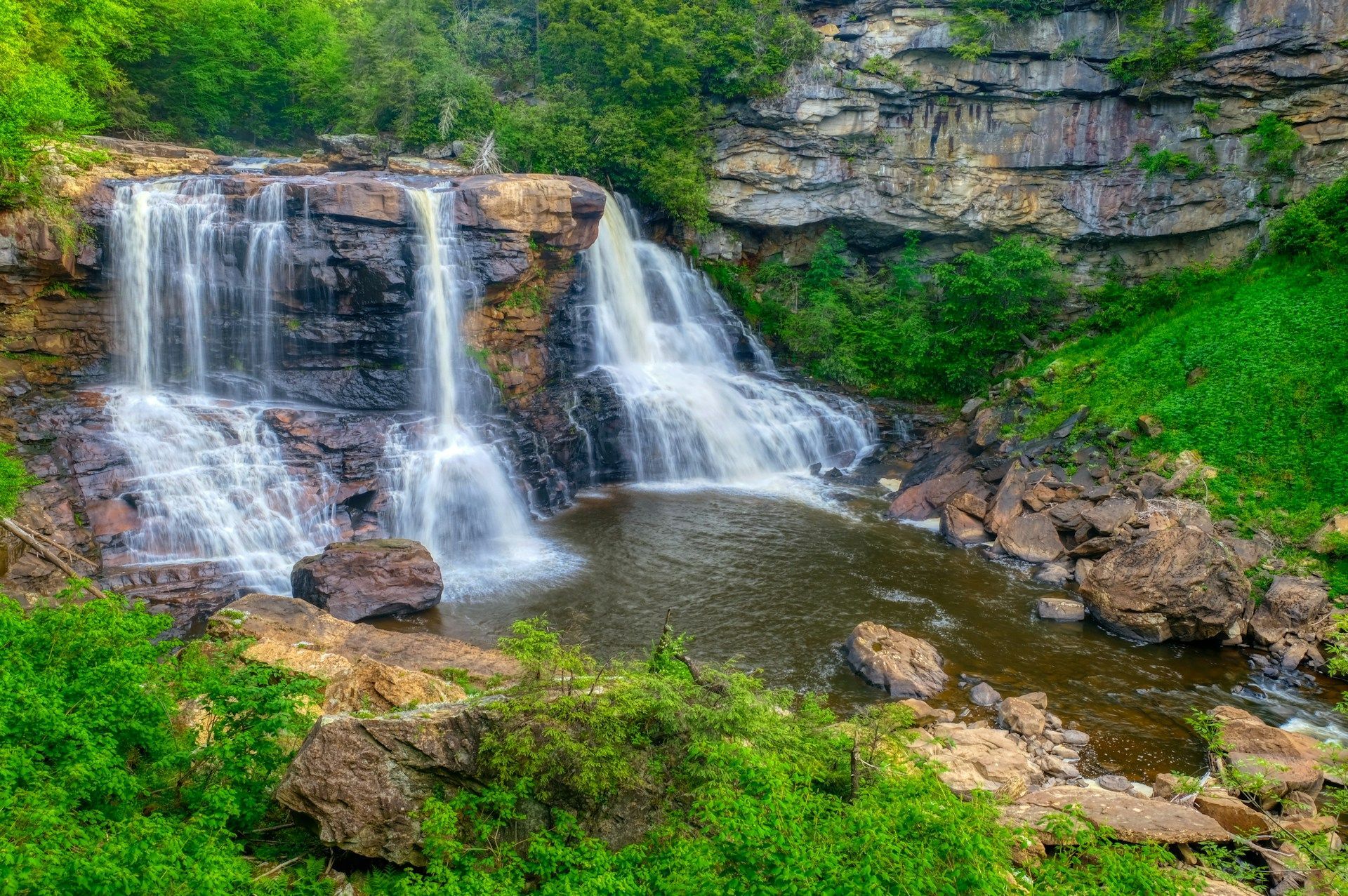 Waterfall cascading over rocky ledges into a pool, surrounded by lush green vegetation.