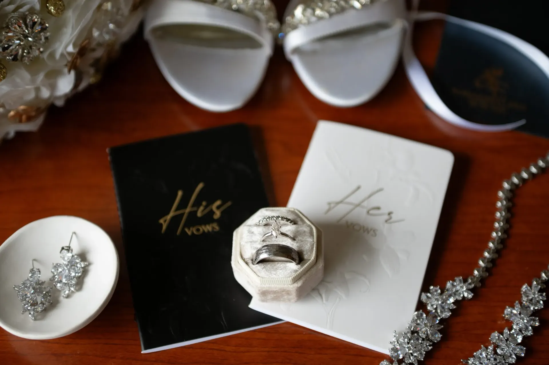 Wedding invitation suite with black and white cards, silver rings, jewelry, and floral accents on a wooden table