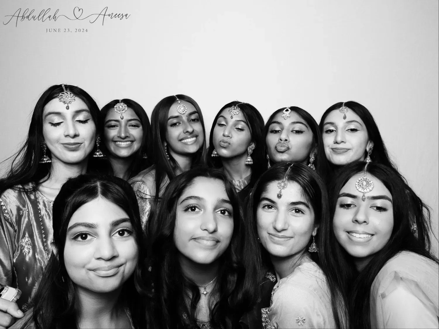 Ten women posing closely together and smiling for a group photo, with decorative forehead jewelry and light tops
