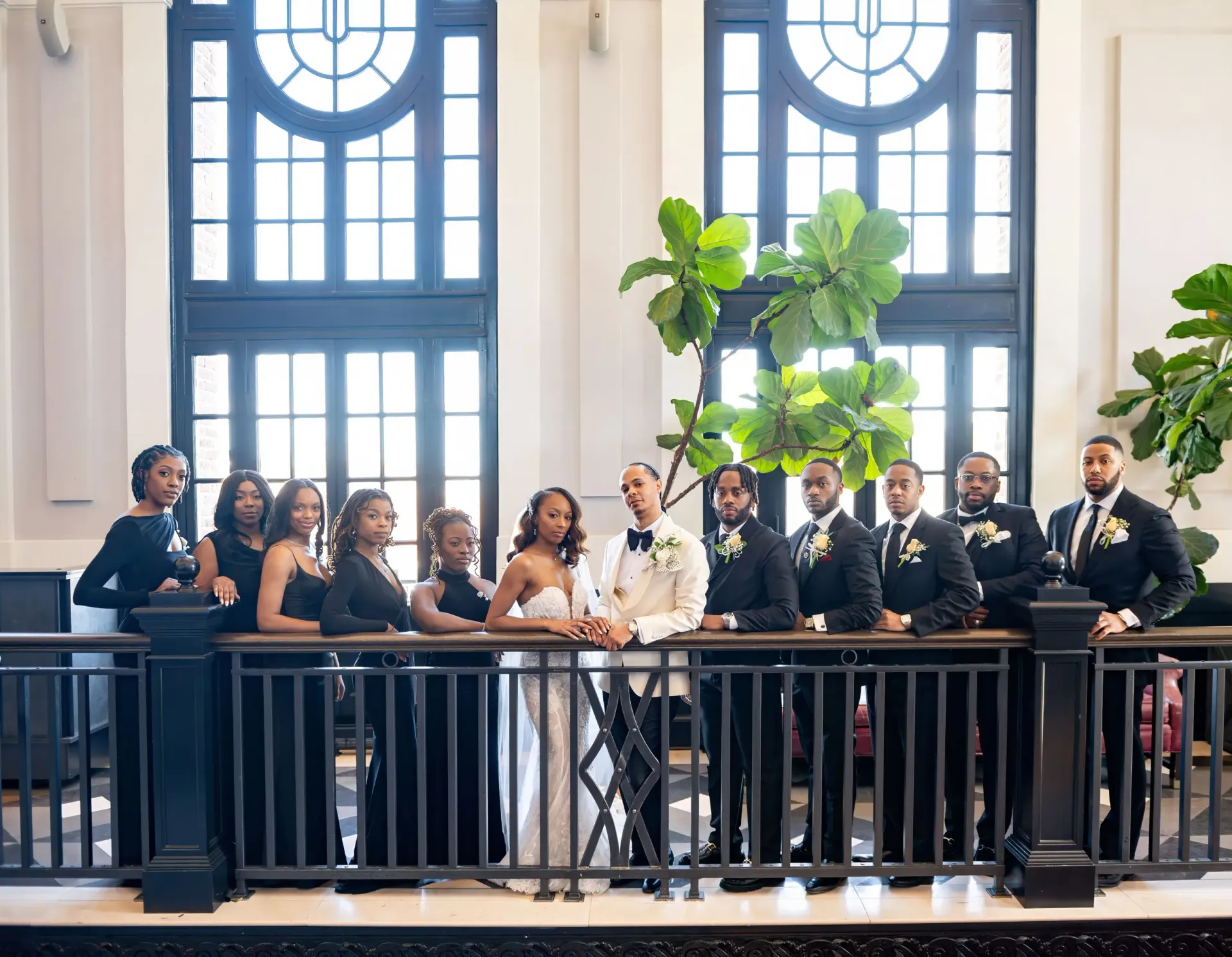 Group of people standing behind a black railing in a bright hall with tall arched windows