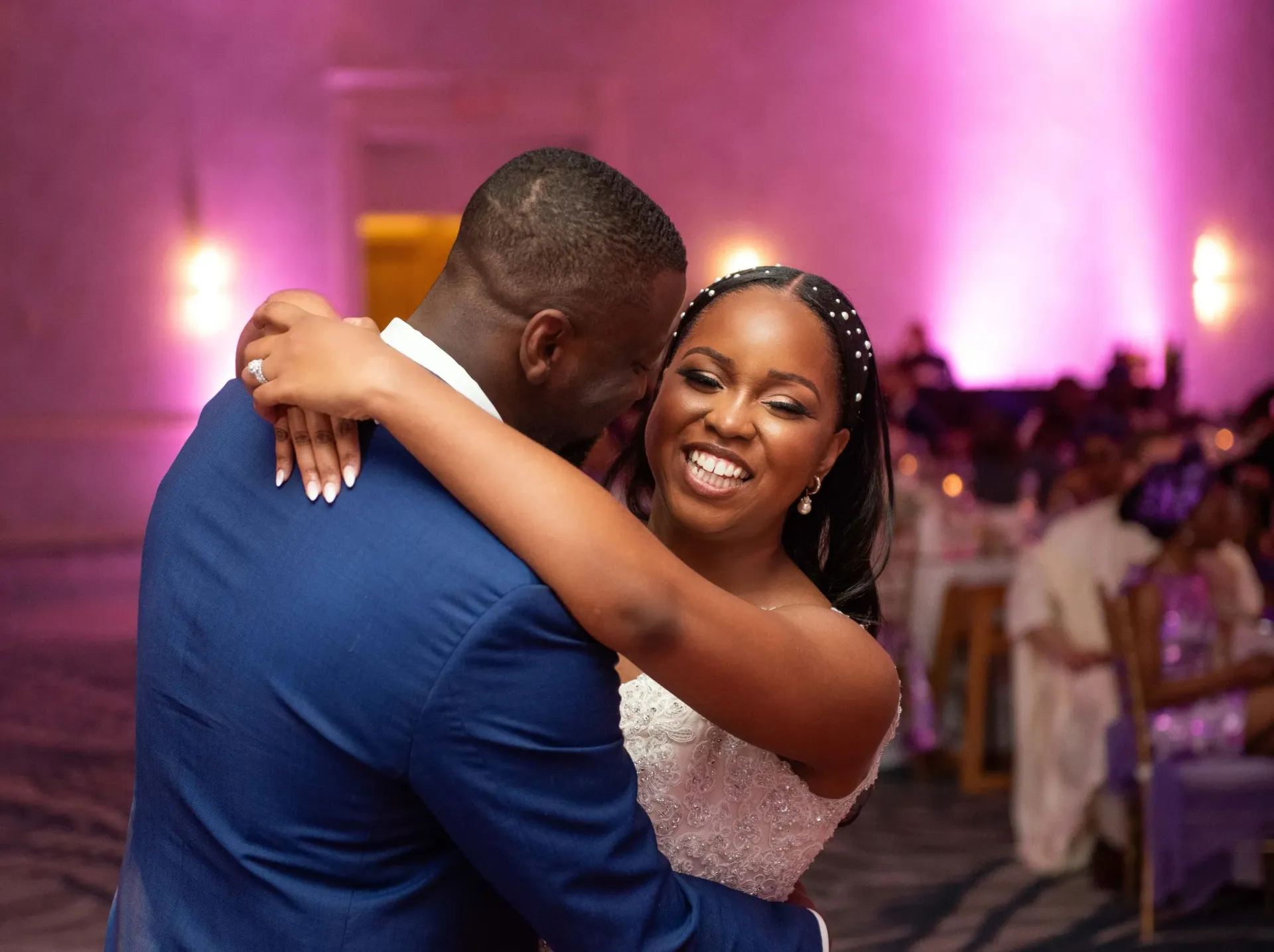 Two people dancing and smiling at a formal event with purple lighting and blurred guests in the background