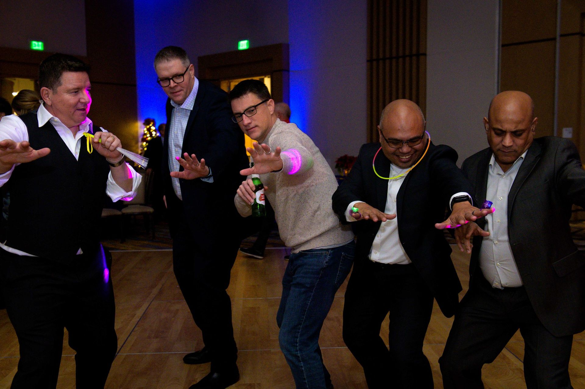 Five men in a dim room aim glowing toy guns during a playful activity.
