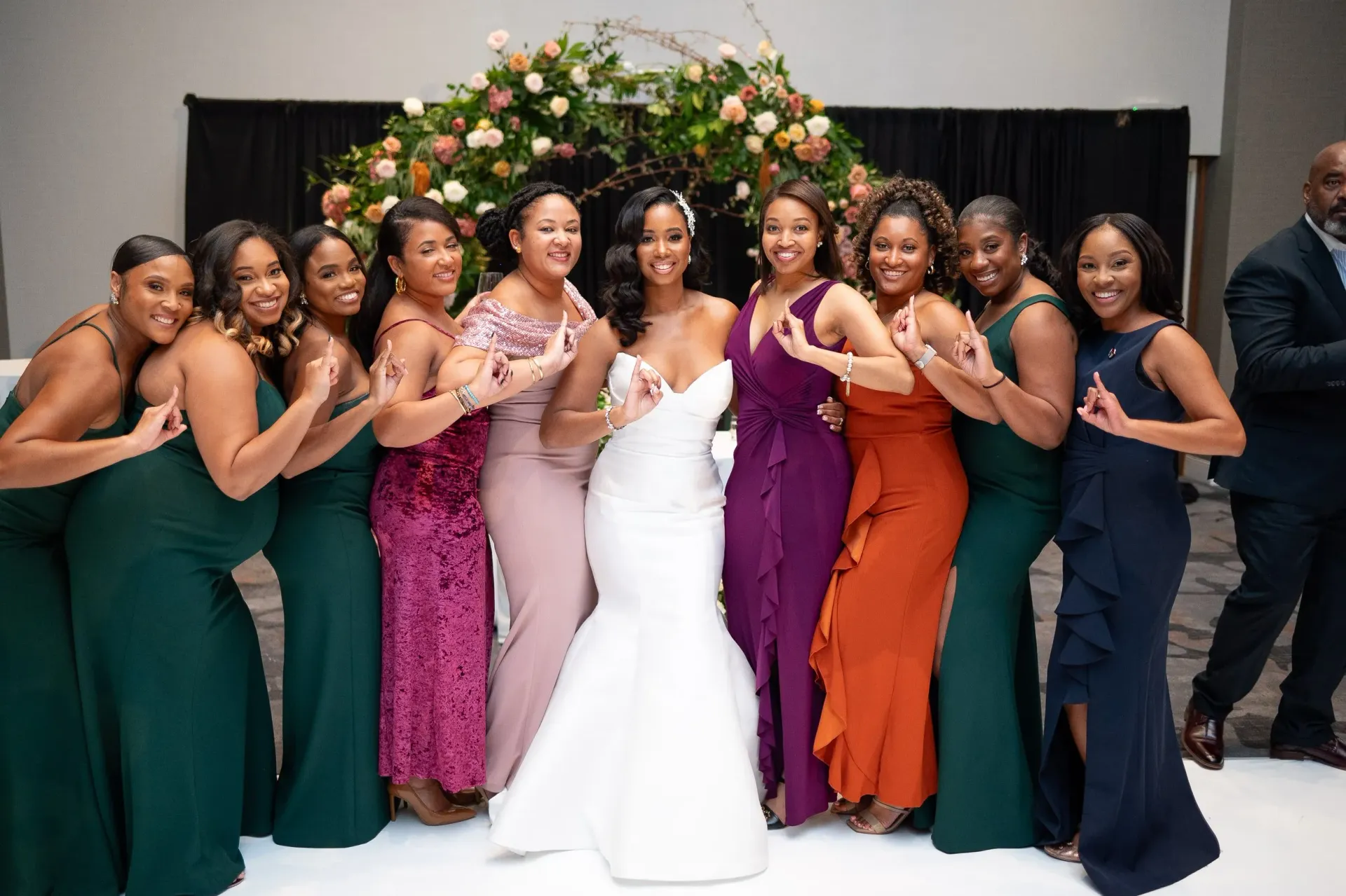 Bridal party posing together in colorful dresses beside a bride in a white gown