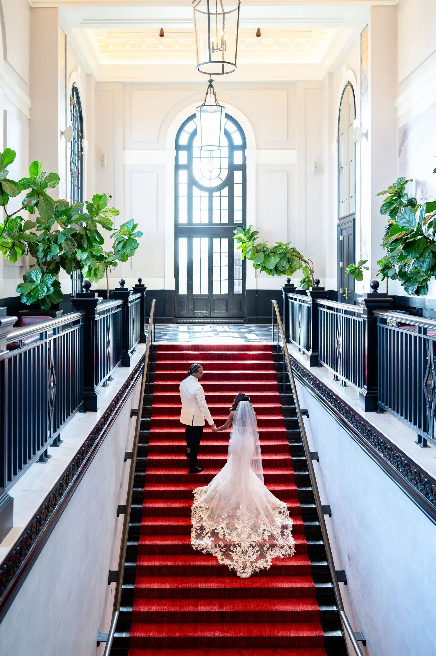 Couple walking up a red-carpeted staircase in a grand, bright hall
