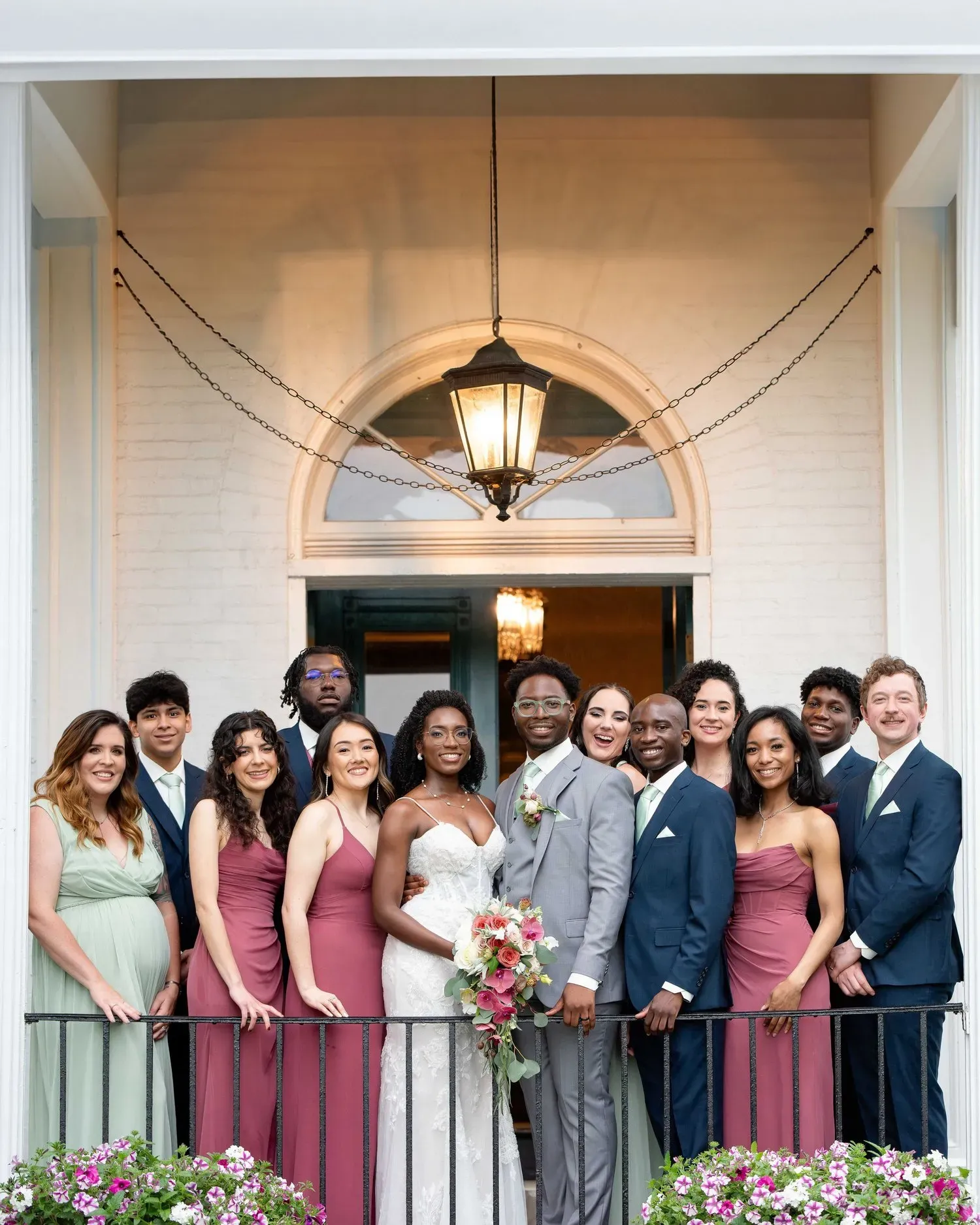 Wedding party posing on a porch under a hanging lantern, with the couple centered among guests.