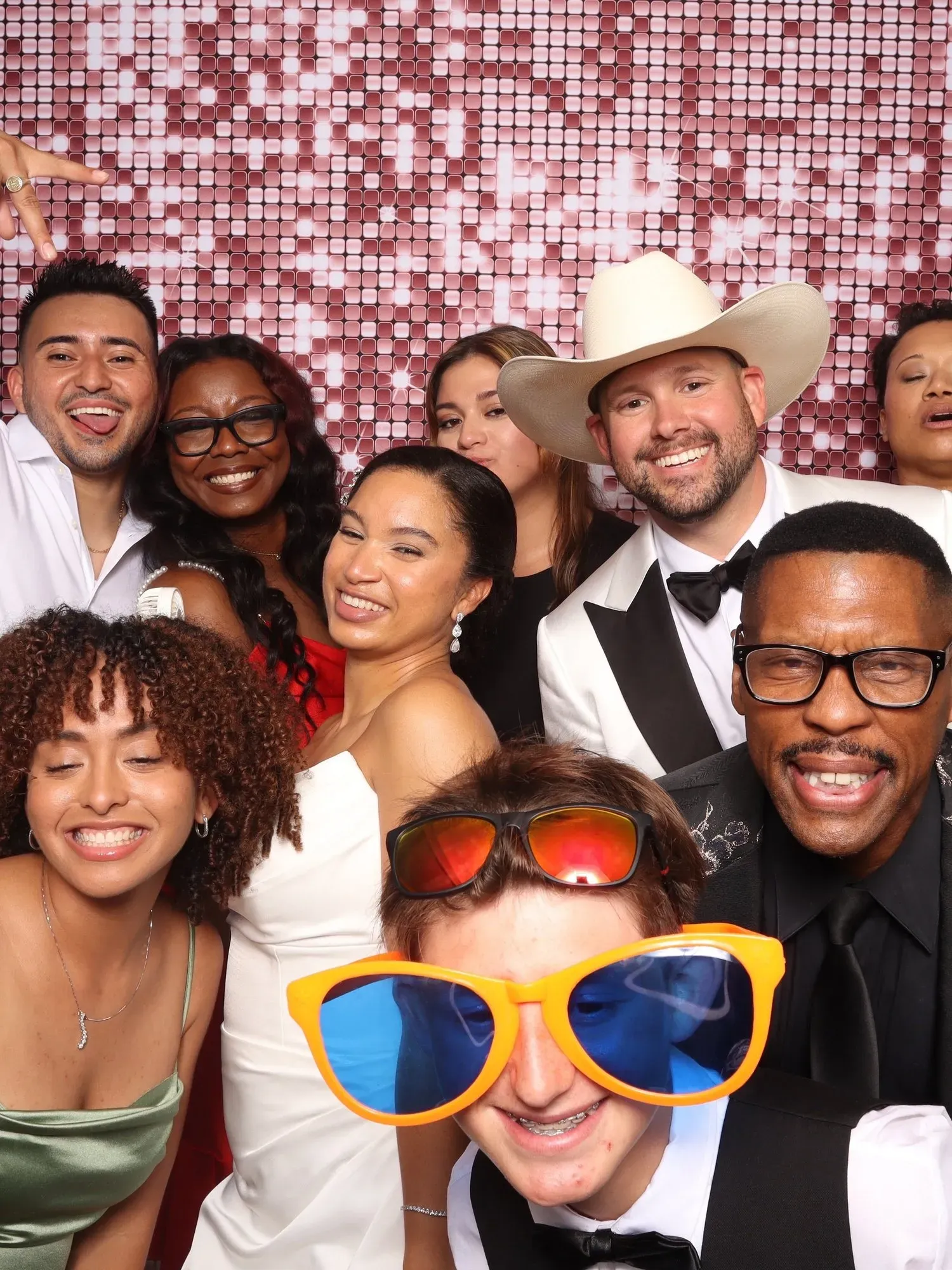 Group selfie at a lively party, with smiling faces, bright oversized glasses, and a pink sequin backdrop