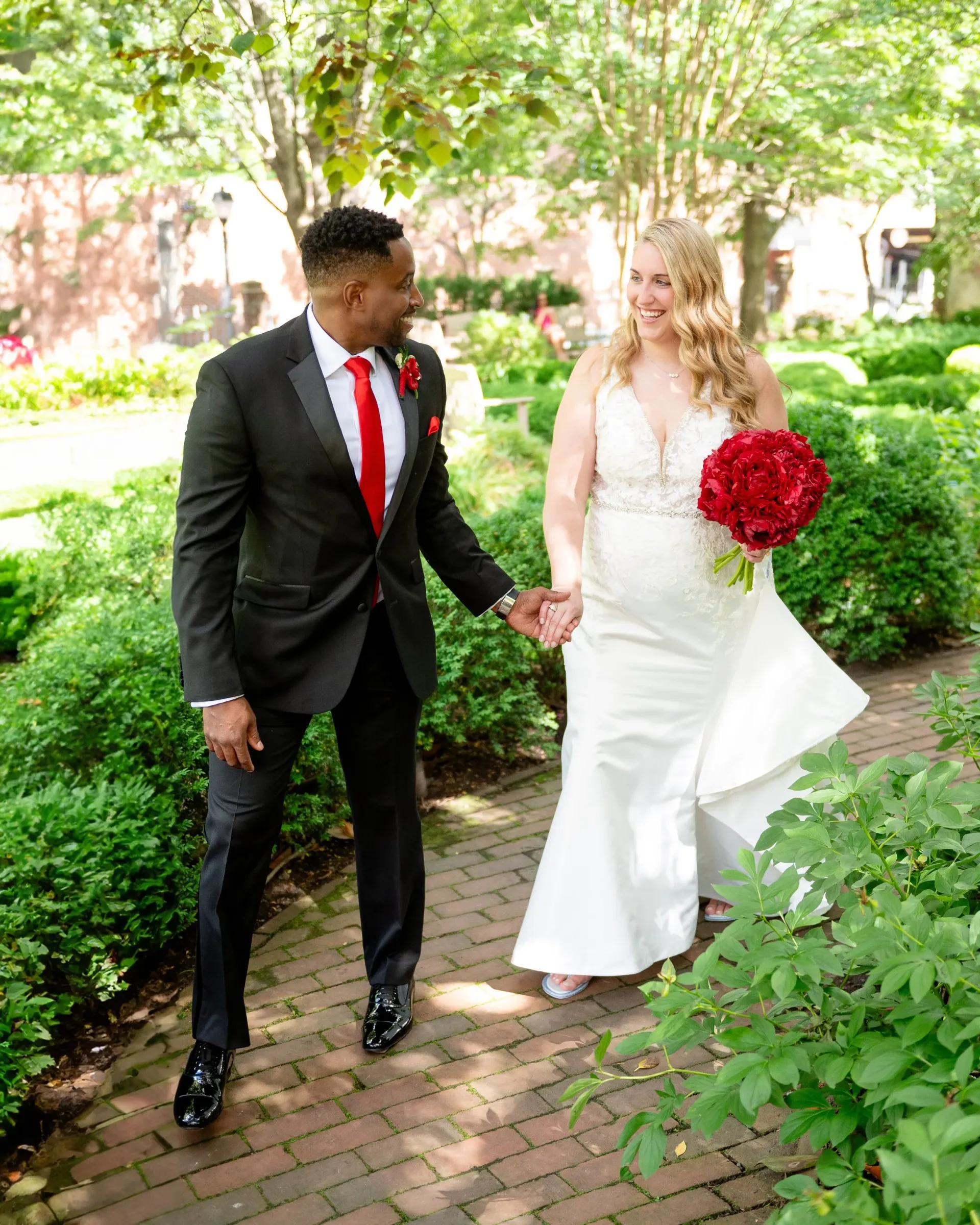 Bride and groom in wedding attire holding hands and walking along a garden path