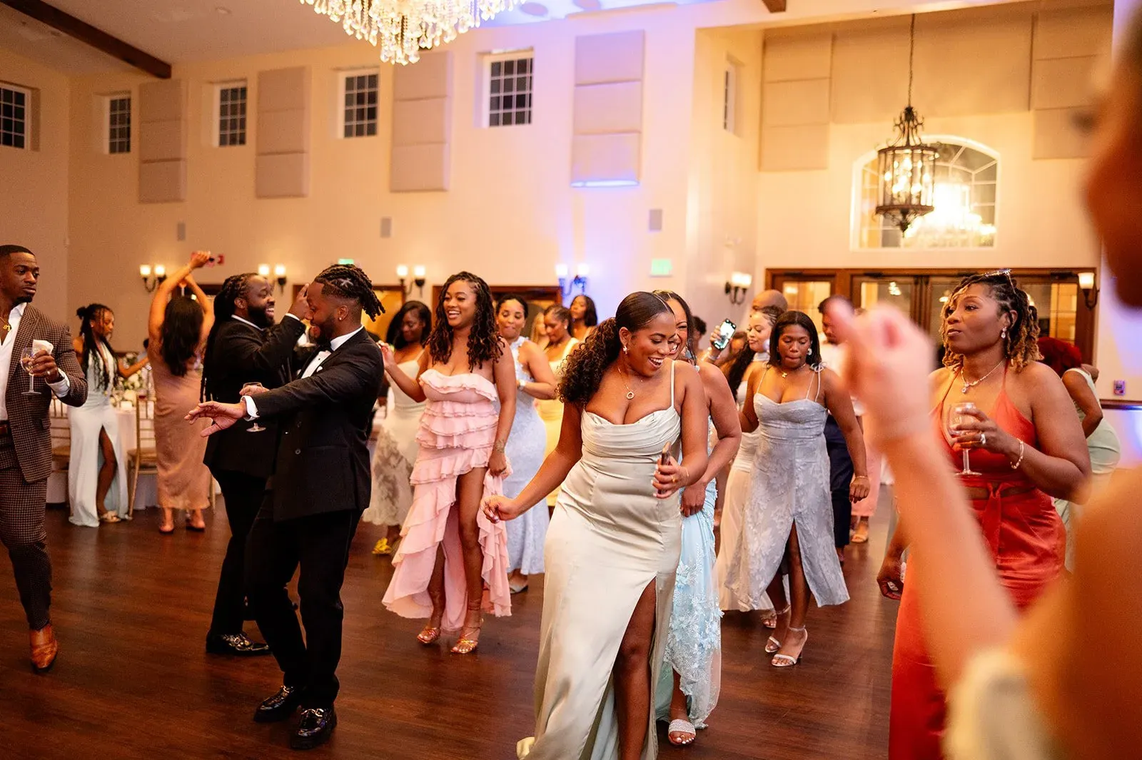 Guests dancing at a warmly lit indoor celebration, with a bride in a white dress at center.