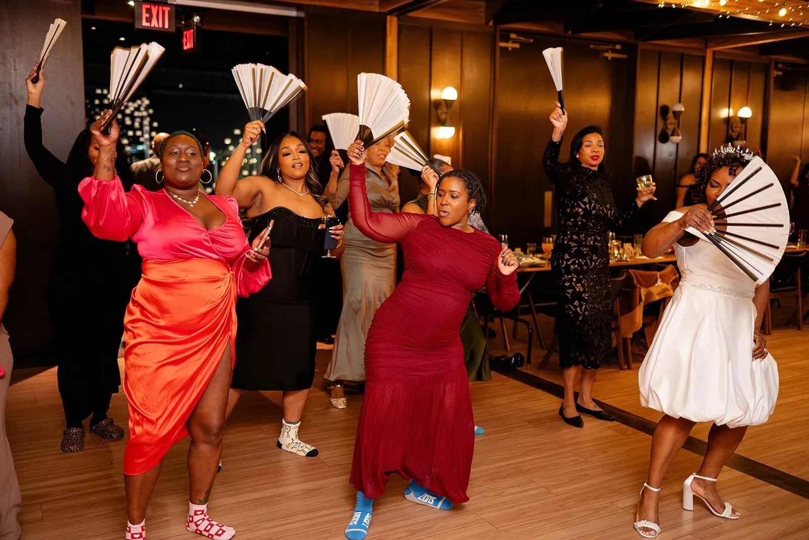 People dancing with fans in a warmly lit indoor venue, some in red and white dresses.