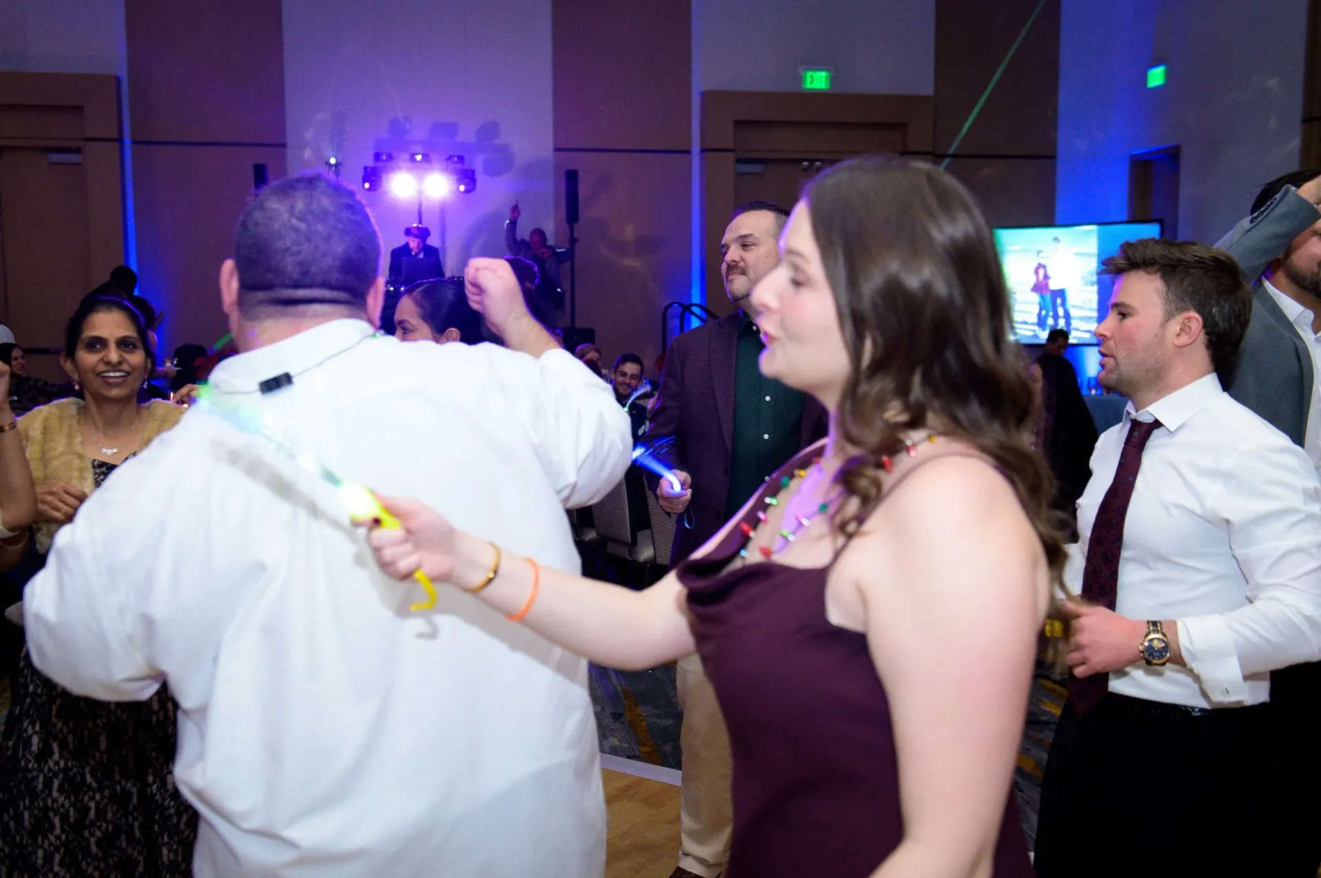 Guests dancing at a dimly lit party, with a woman in a purple dress in the foreground.