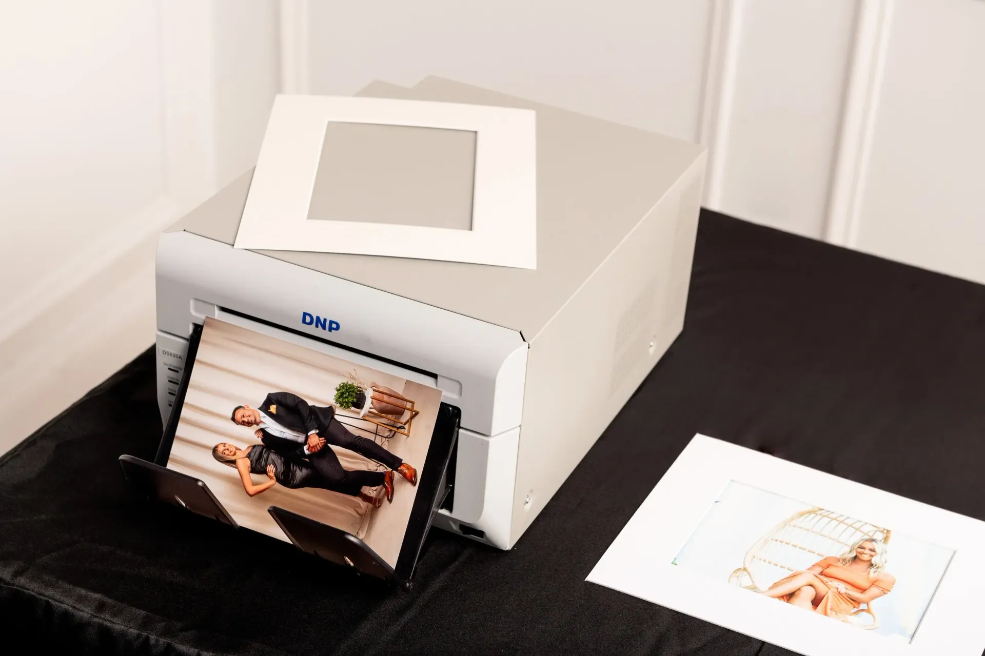 Photo printer printing a small photo on a black table, with another print beside it