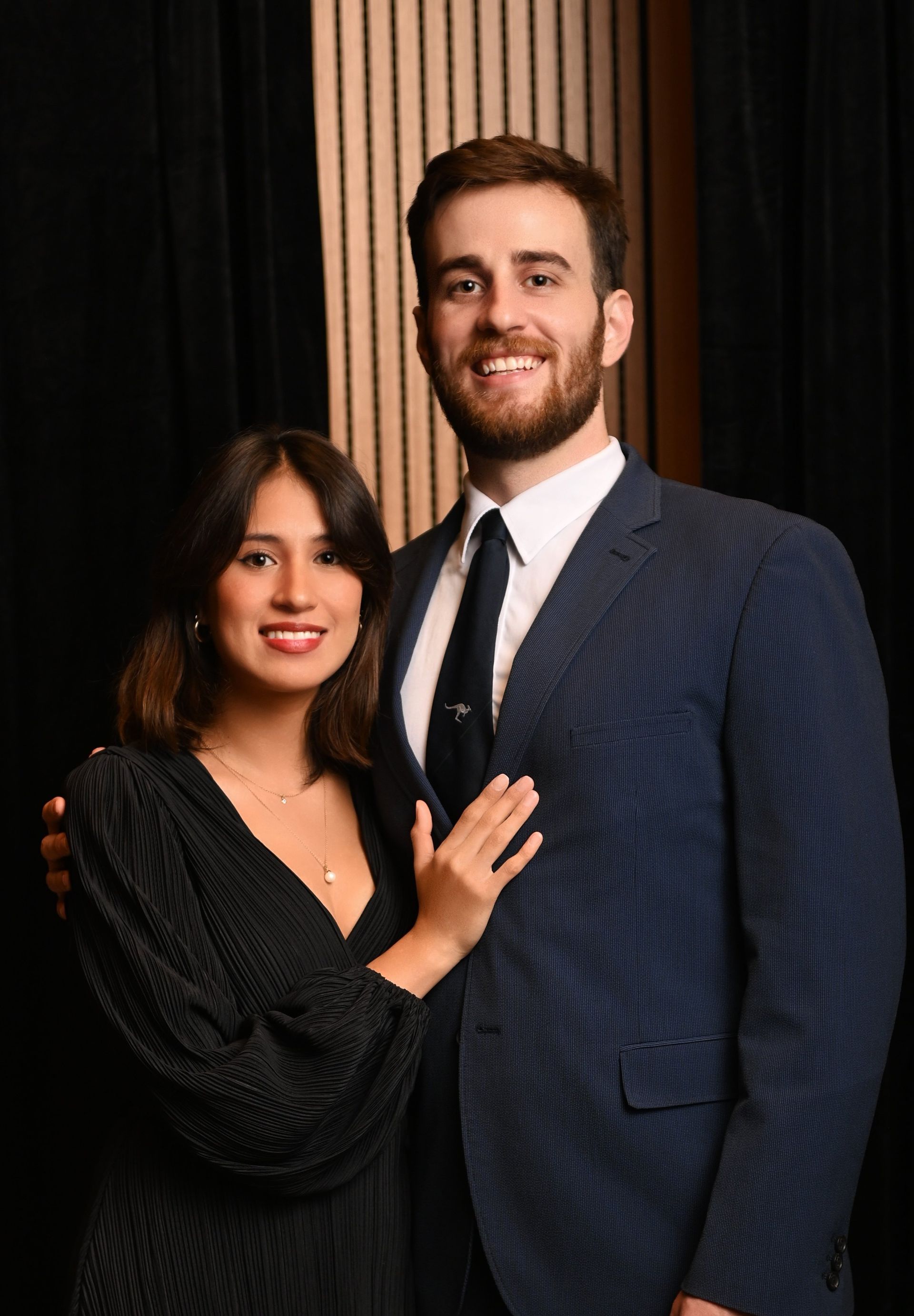 Two people posing together in formal attire against a dark backdrop