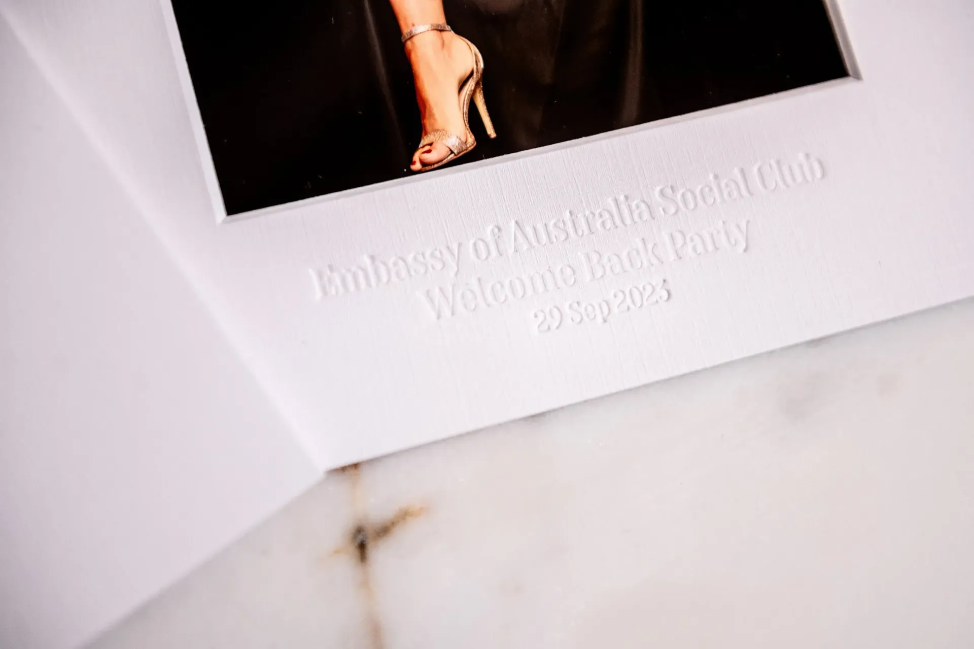 Close-up of a glossy brochure with a partially visible model and embossed text on a white marble surface