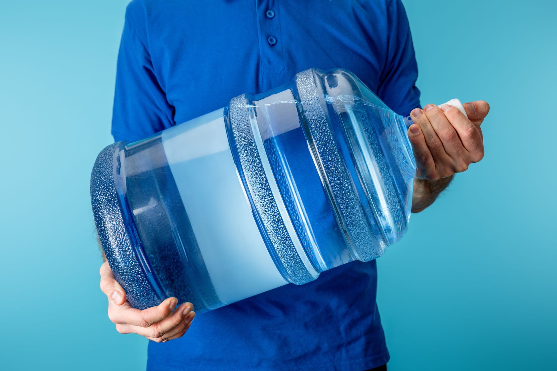 Un hombre con una camisa azul sostiene una botella grande de agua.