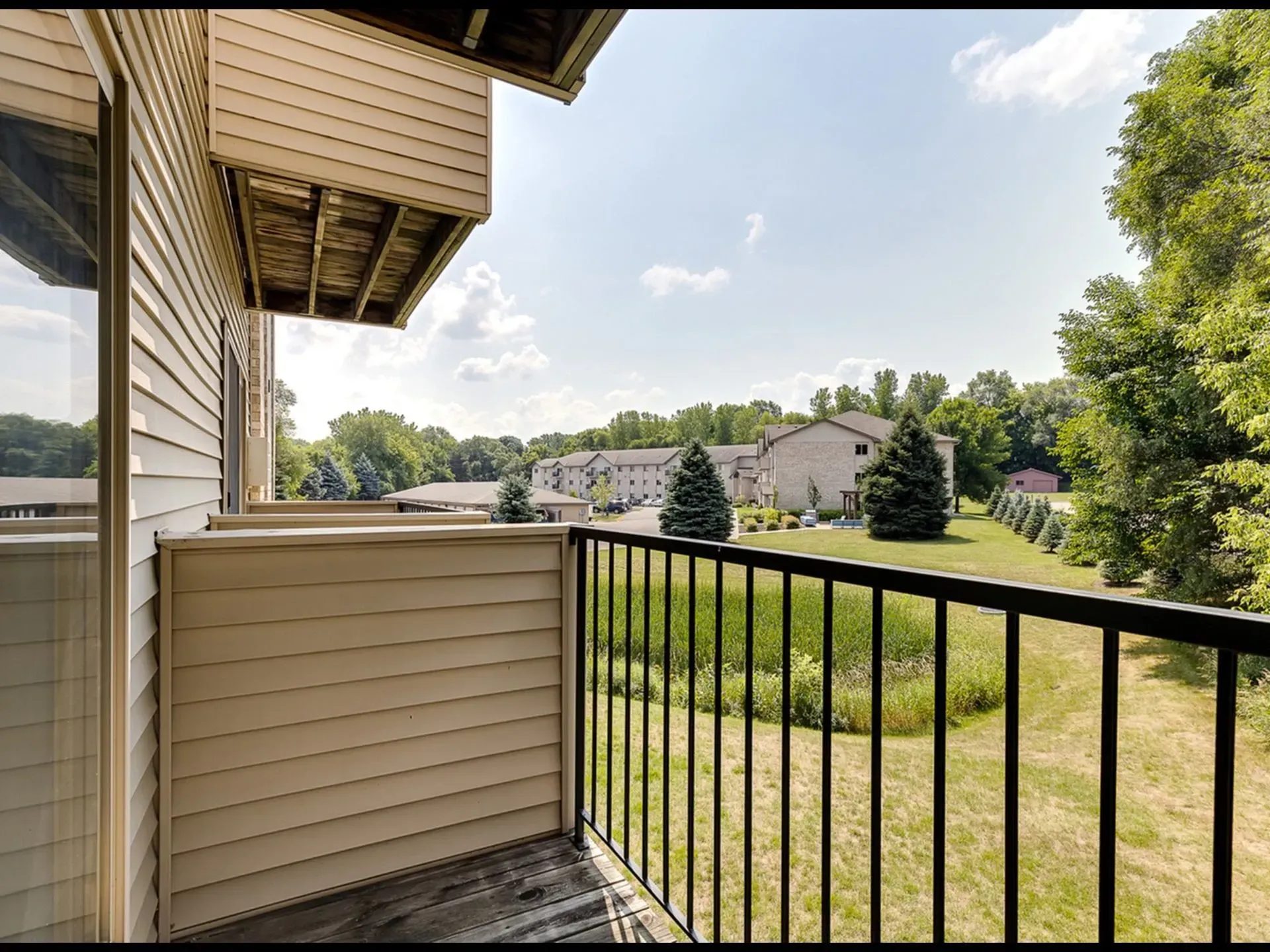 View from a balcony overlooking a grassy area with trees and apartment buildings in the background.