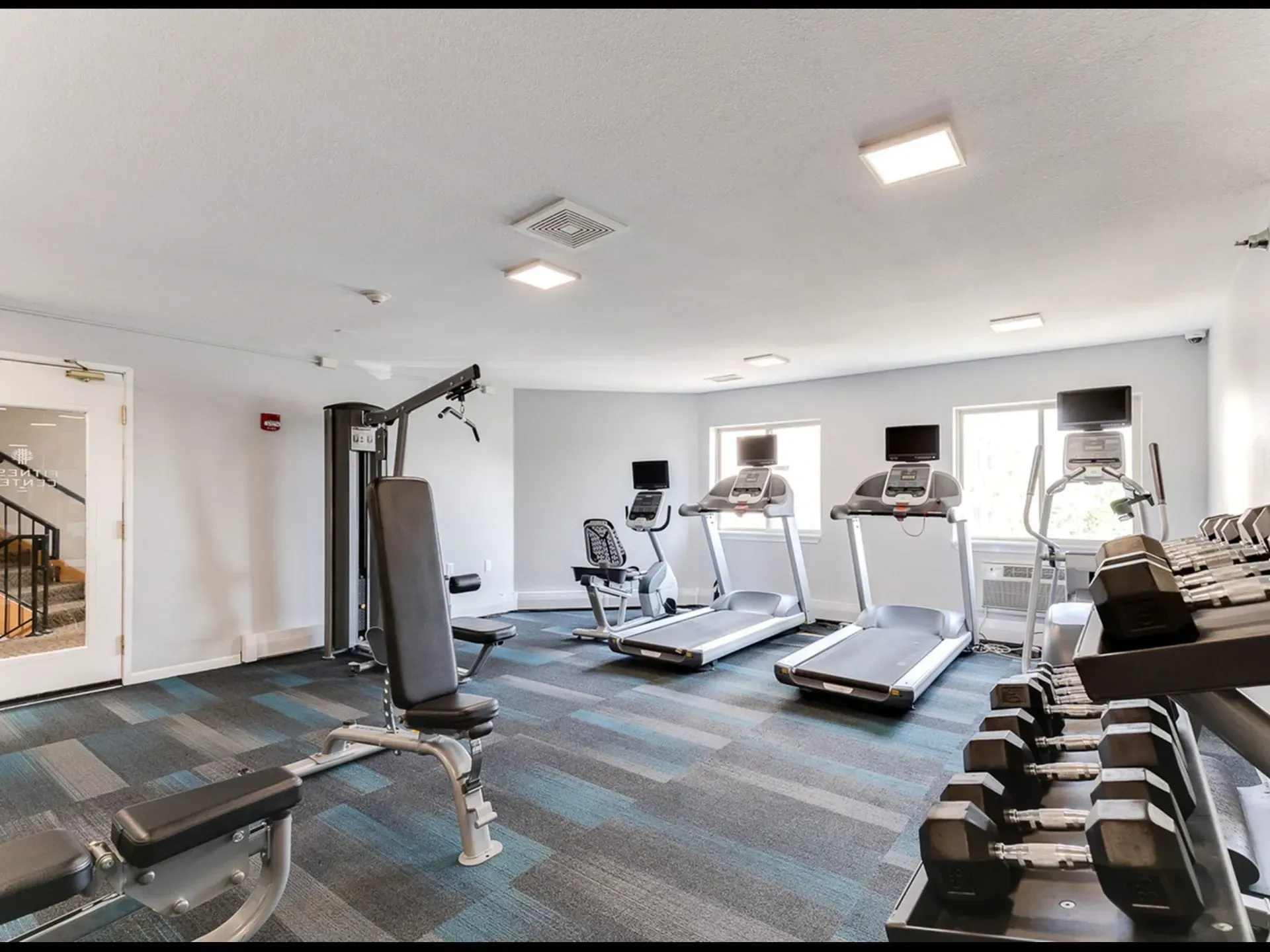 Fitness center with treadmills, elliptical, weight machine, and dumbbells.