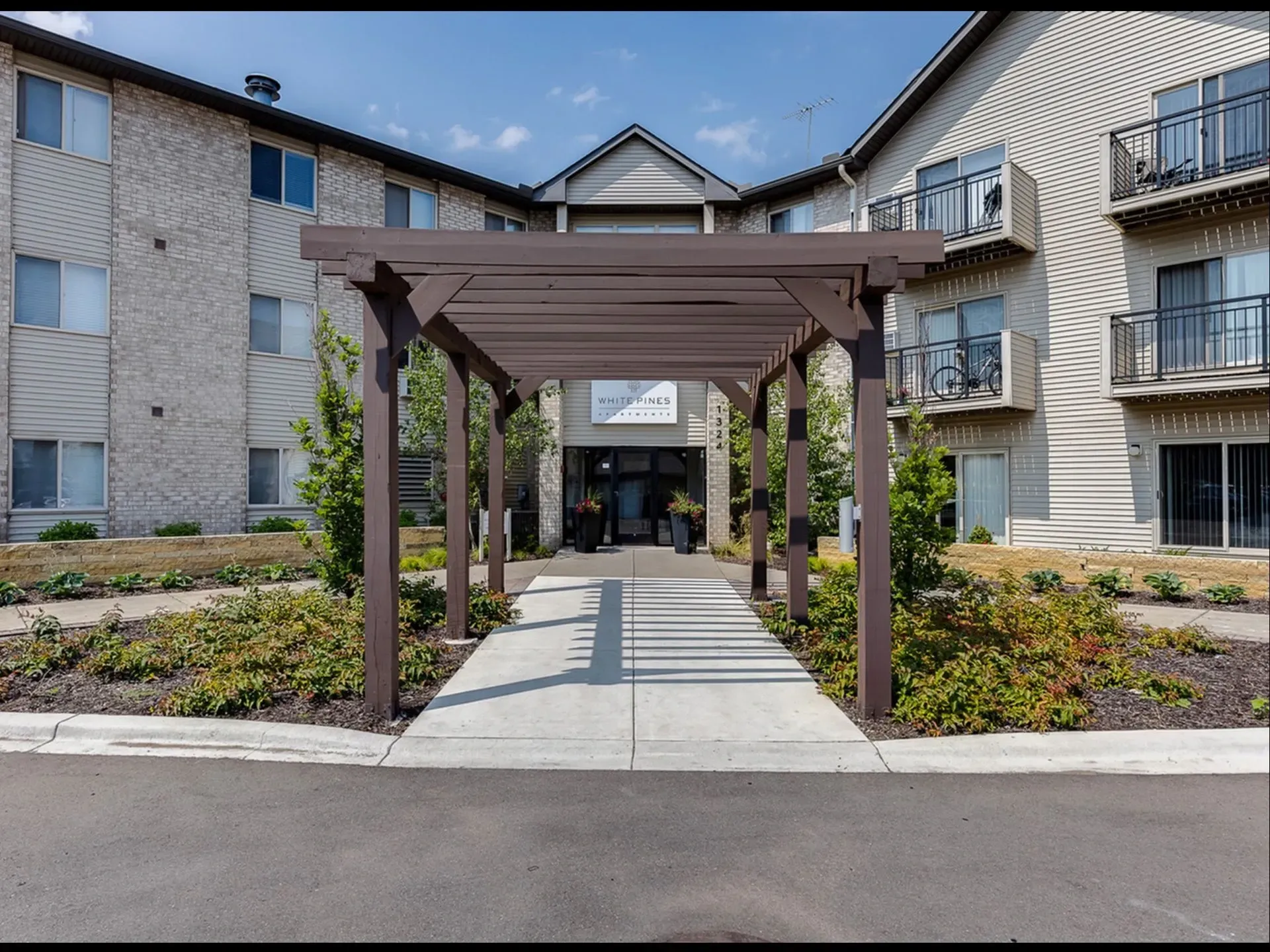 Entrance to White Pines Apartments with a wooden pergola and landscaping.