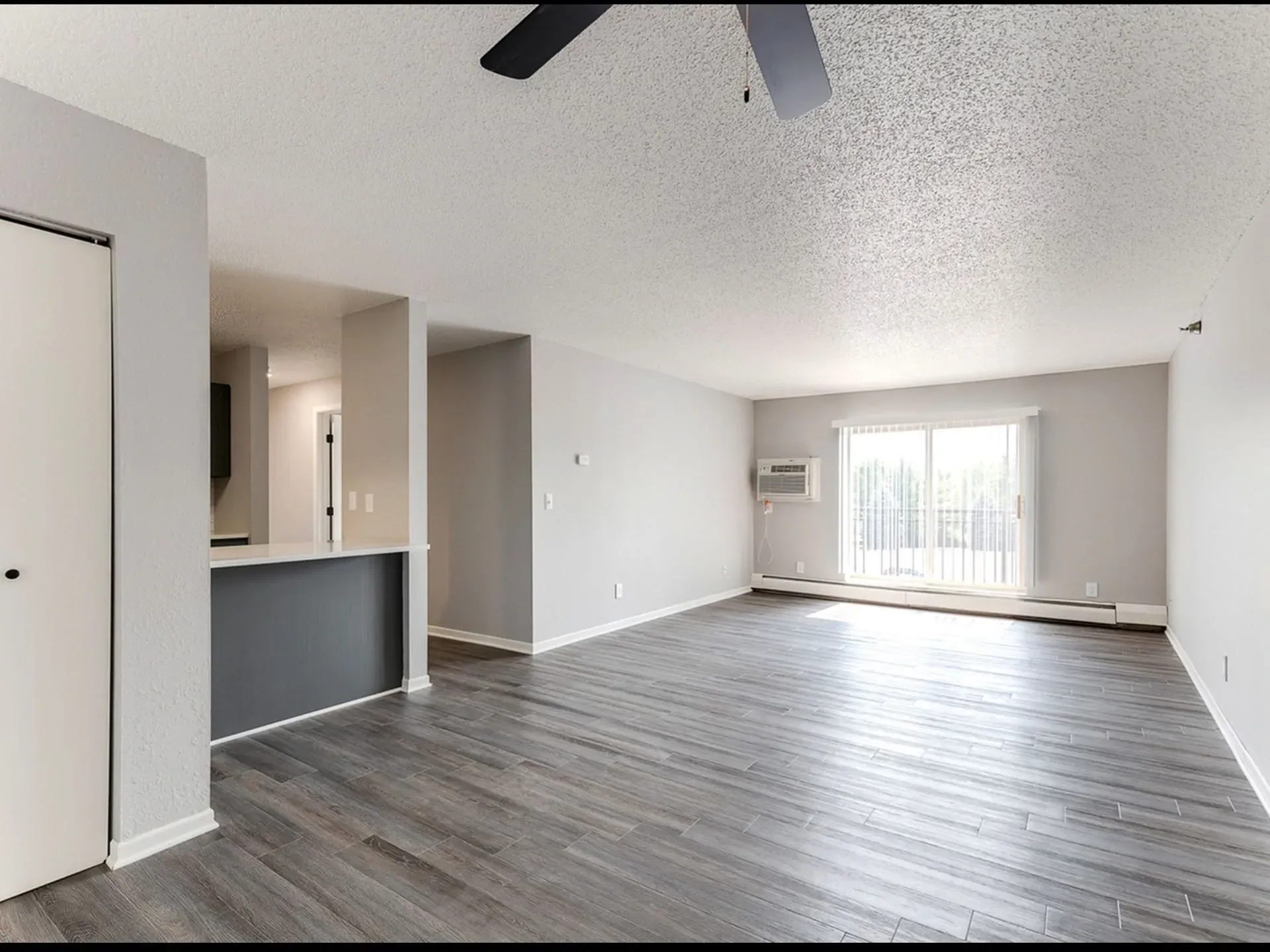 Spacious living room with a ceiling fan, large sliding glass door, and a breakfast bar.