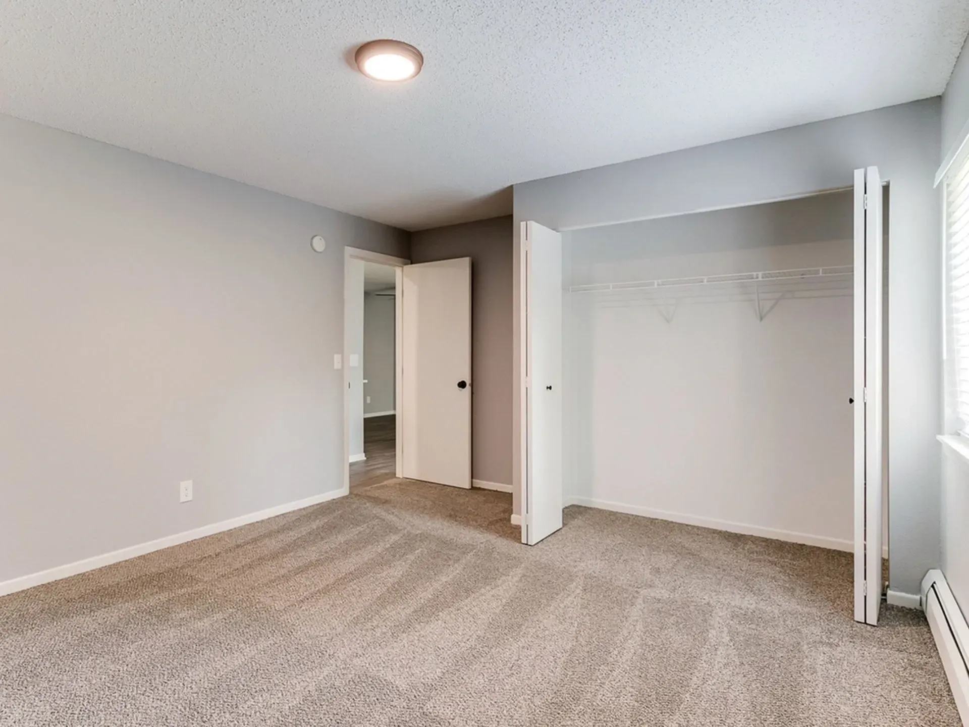 Interior view of a vacant bedroom with neutral gray walls, a large closet with bifold doors, and neutral carpeting.