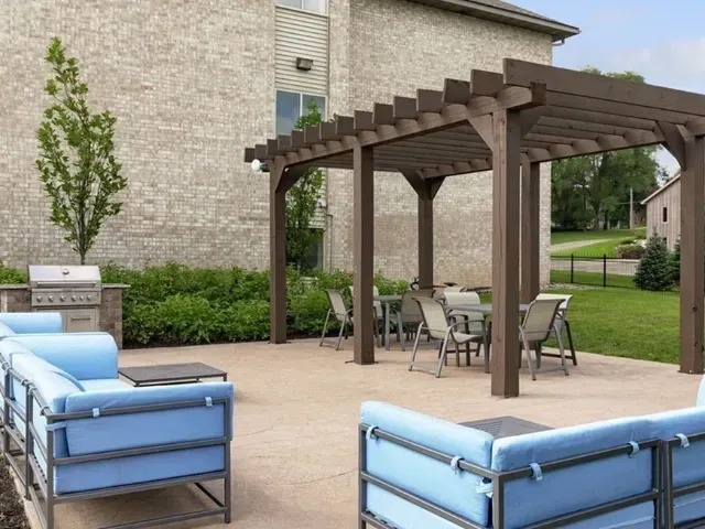 Outdoor patio with a pergola, dining tables, seating, and a built-in grill.