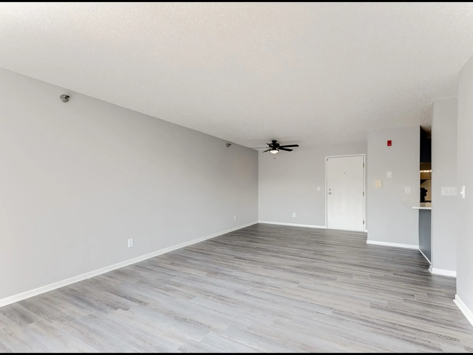 Empty living room with grey walls, a ceiling fan, and a door.