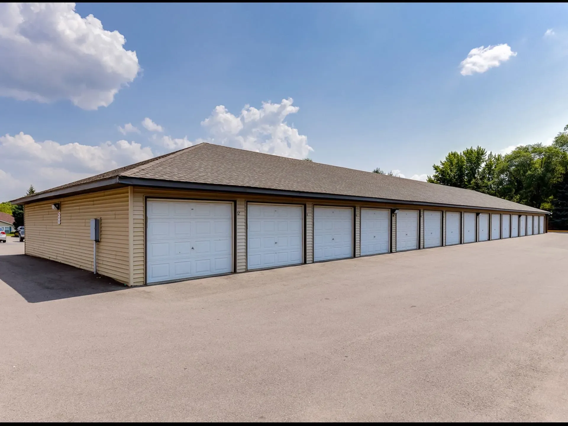 Row of beige buildings with white garage doors under a cloudy blue sky