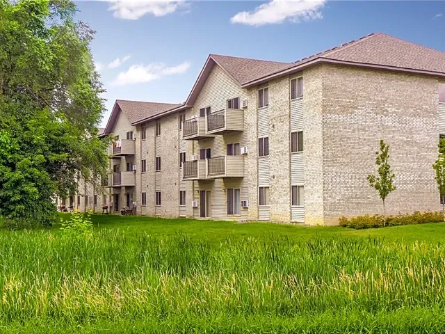 Exterior view of a brick apartment building with balconies and green lawn.