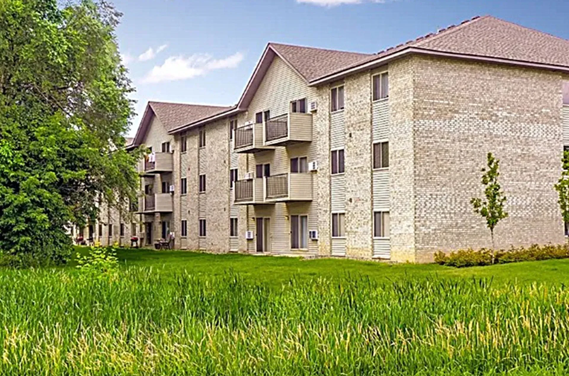 Exterior view of a brick apartment building with balconies and green lawn.