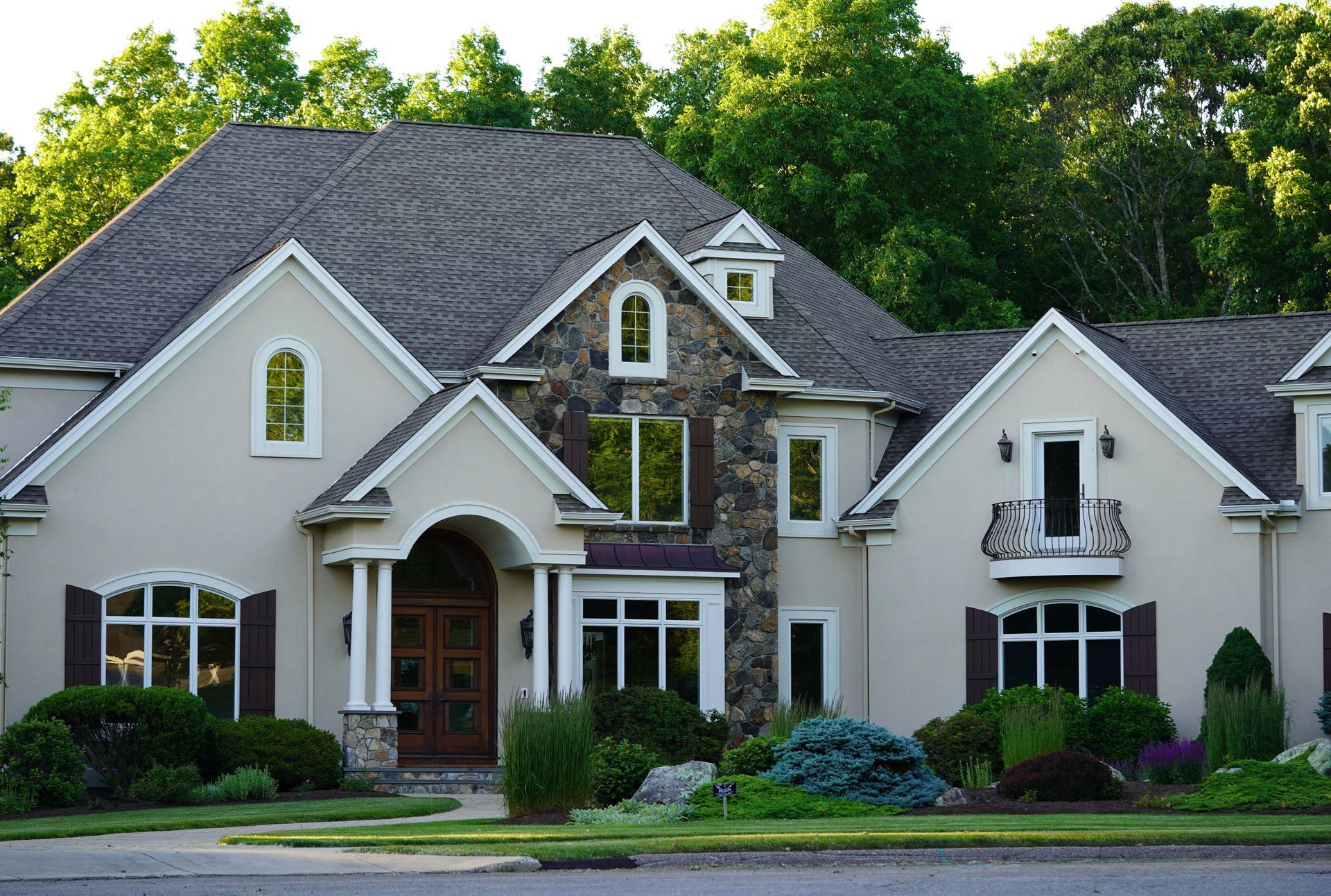 Large beige suburban house with a dark roof, arched entryway, and landscaped front yard.