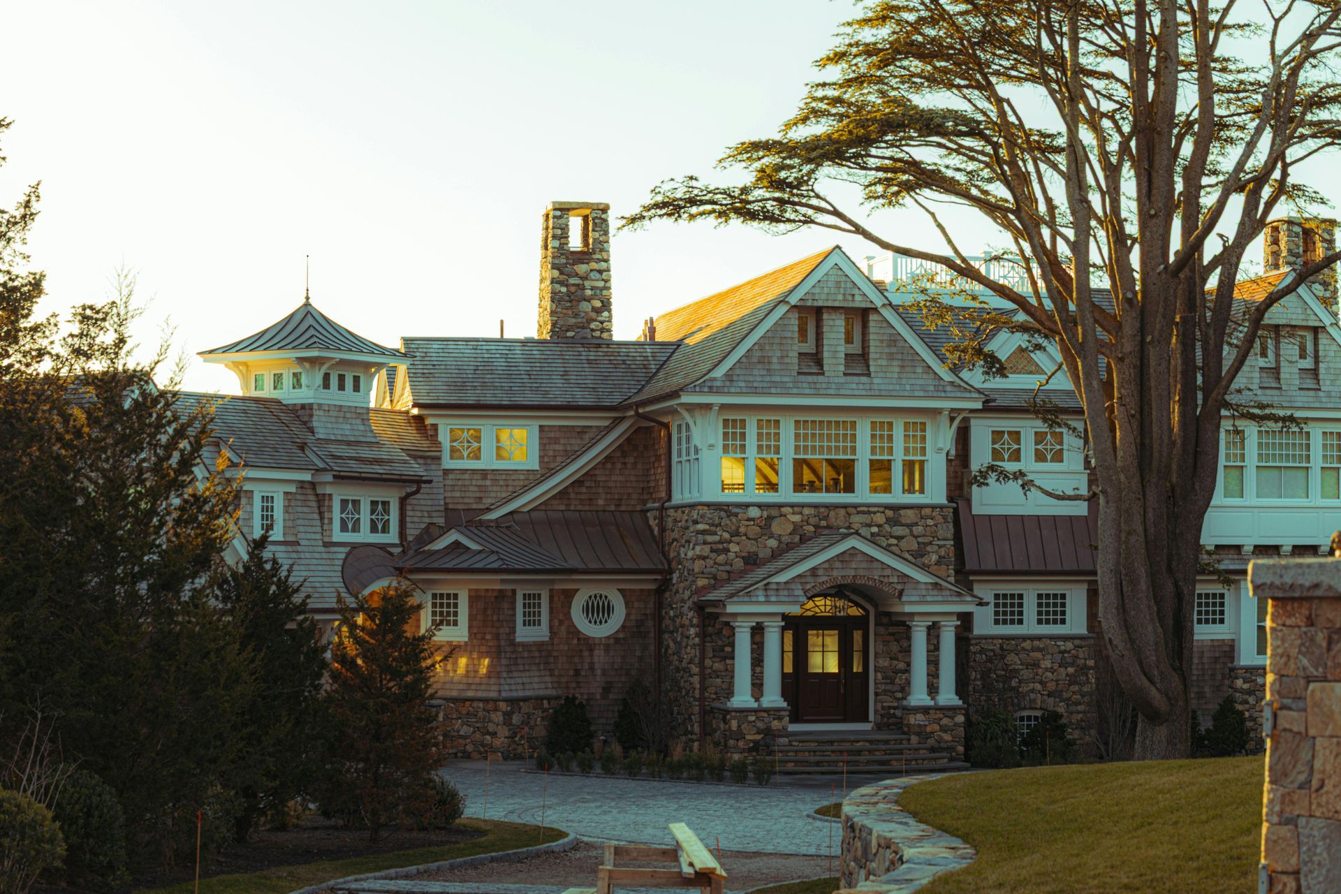 Historic brick mansion with white trim and a large tree in the foreground at sunset