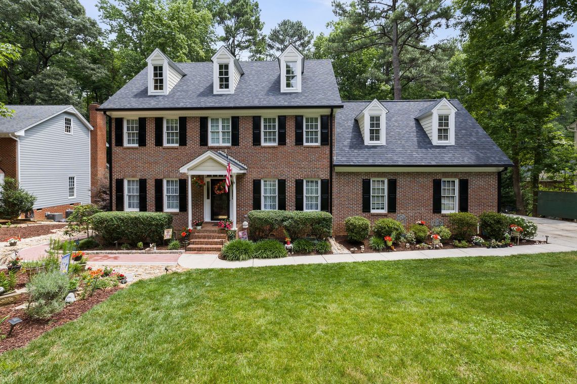 Large brick colonial house with white trim, landscaped yard, and a front walkway