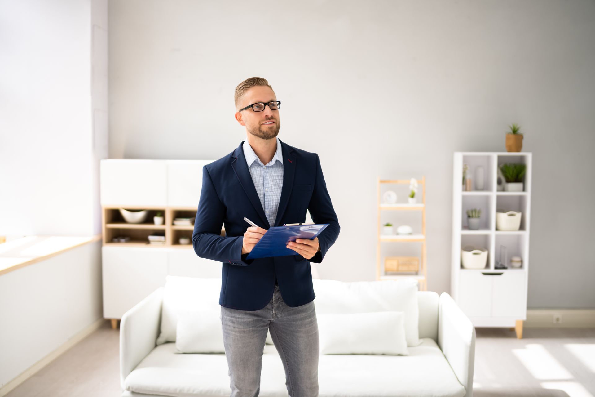 Man in a navy blazer holding a tablet in a bright living room with white furniture