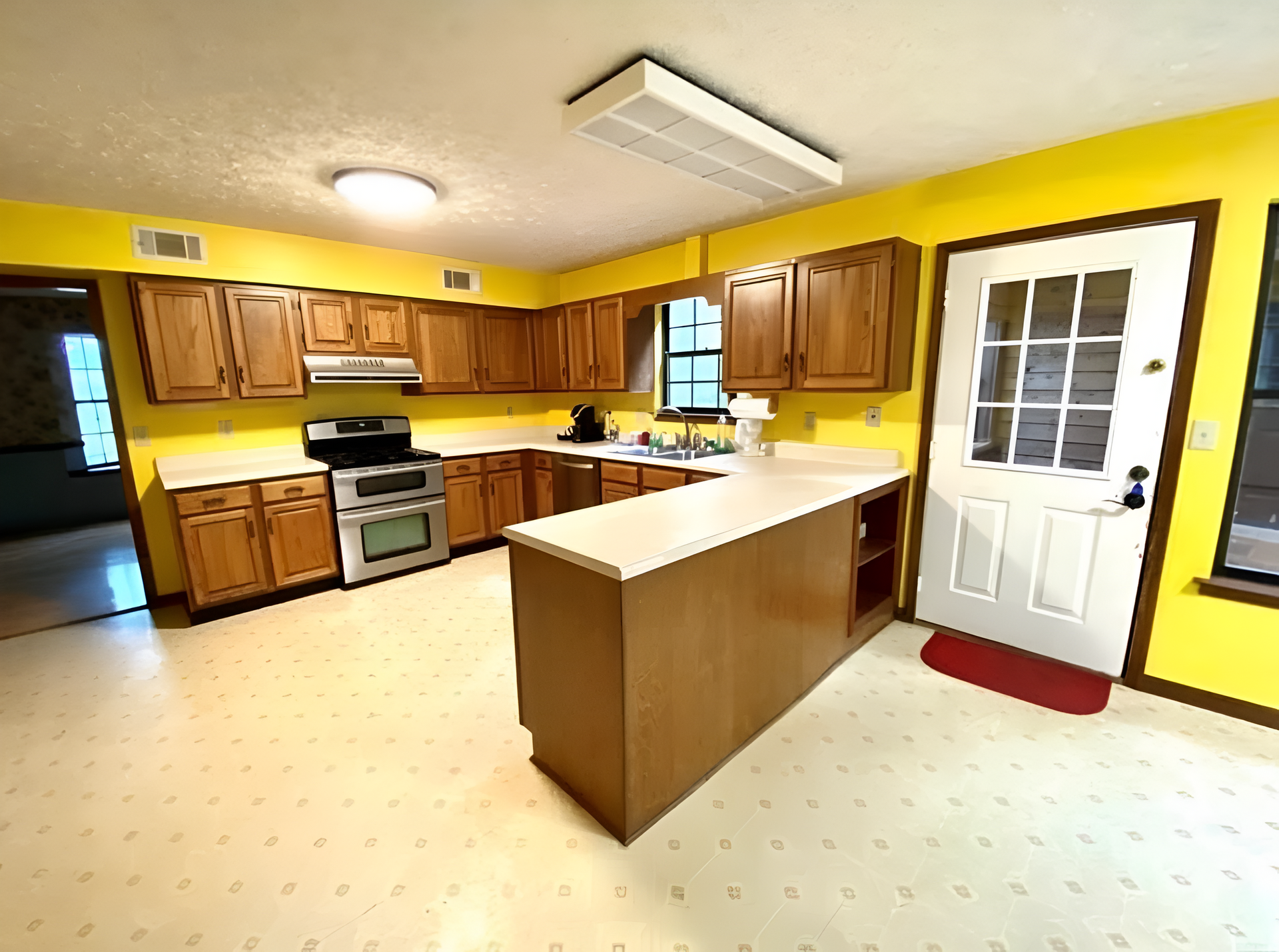 Bright yellow kitchen with wooden cabinets, white island, stove, sink, and back door with window panes