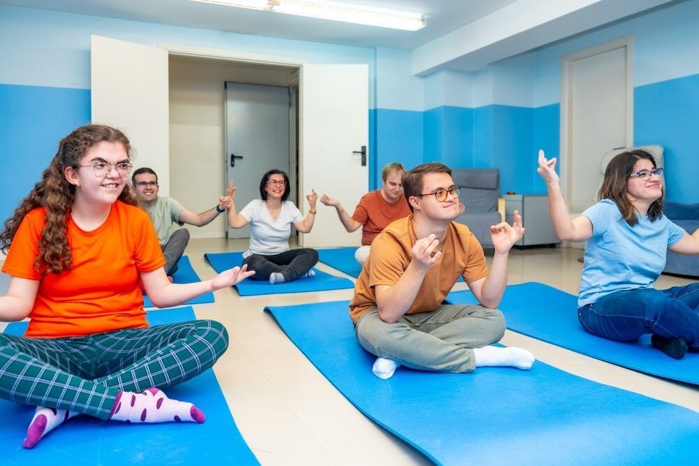 A Group of People Sit Cross-legged on Blue Mats — Adaptive Care Pty Ltd In Geelong, VIC