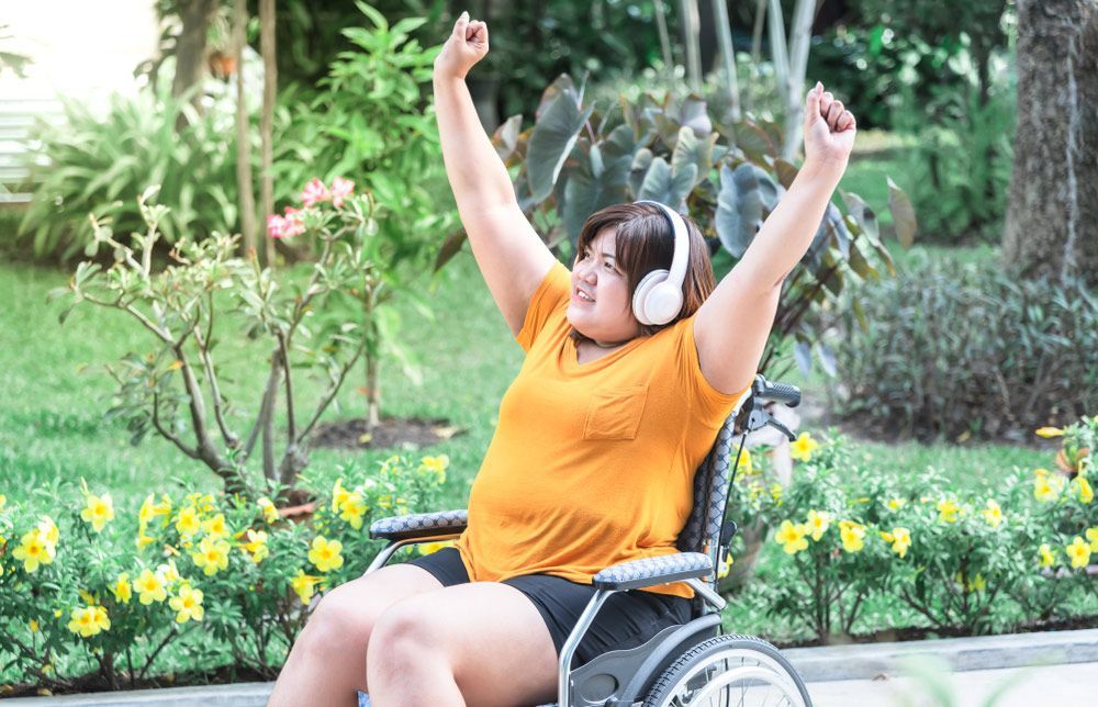 A Woman in a Wheelchair is Wearing Headphones and Dancing — Adaptive Care Pty Ltd In Tarneit, VIC